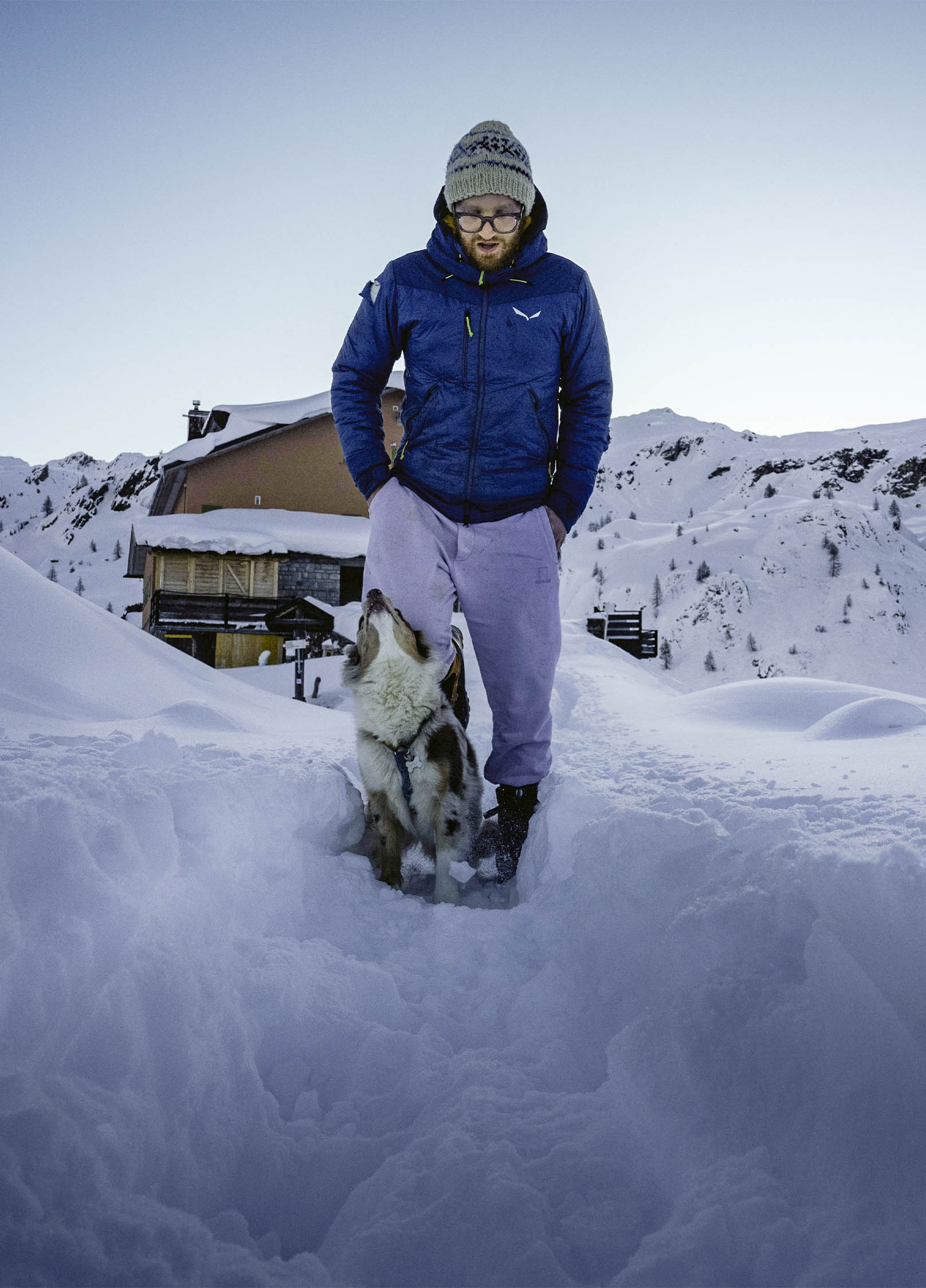 Una persona con un cane davanti al Rifugio Fratelli Calvi innevato